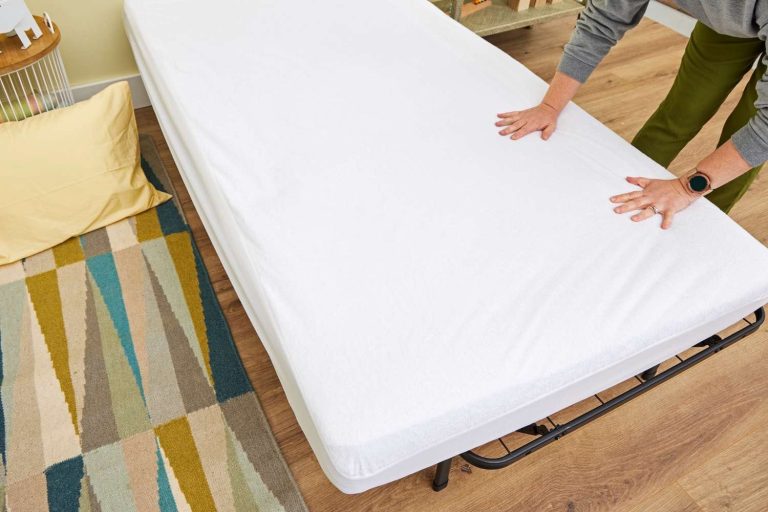 Waterproof mattress protector fitted snugly over a memory foam mattress in a bright bedroom